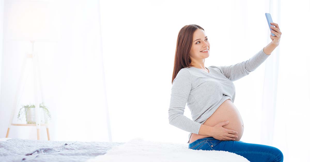 Pregnant woman taking a selfie in her bedroom