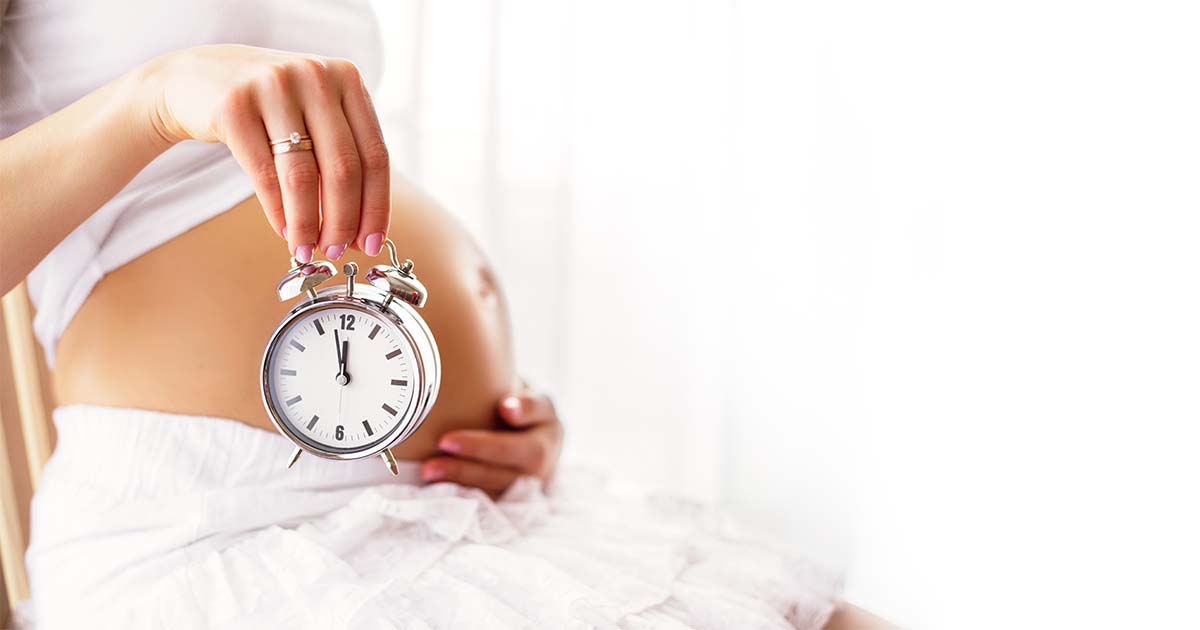 Woman holding a clock next to her pregnant belly