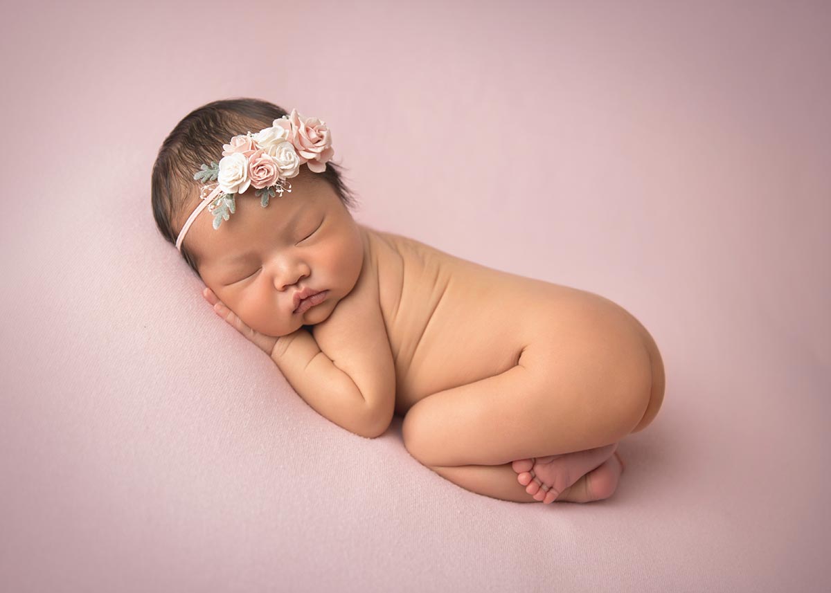 Newborn photo of a girl wearing a beautiful flower headband while sleeping on her side