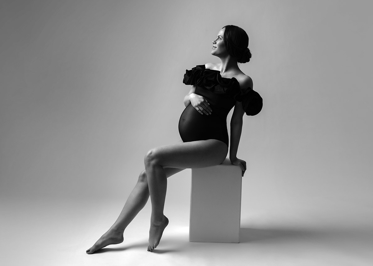 Pregnant mother sitting on a block in a photo studio while holding her belly