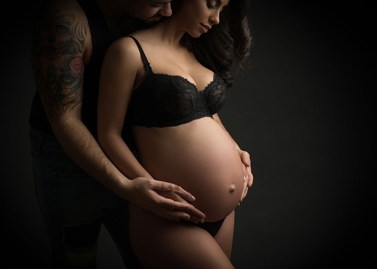 Father with tattooed arms holding his wife's pregnant belly