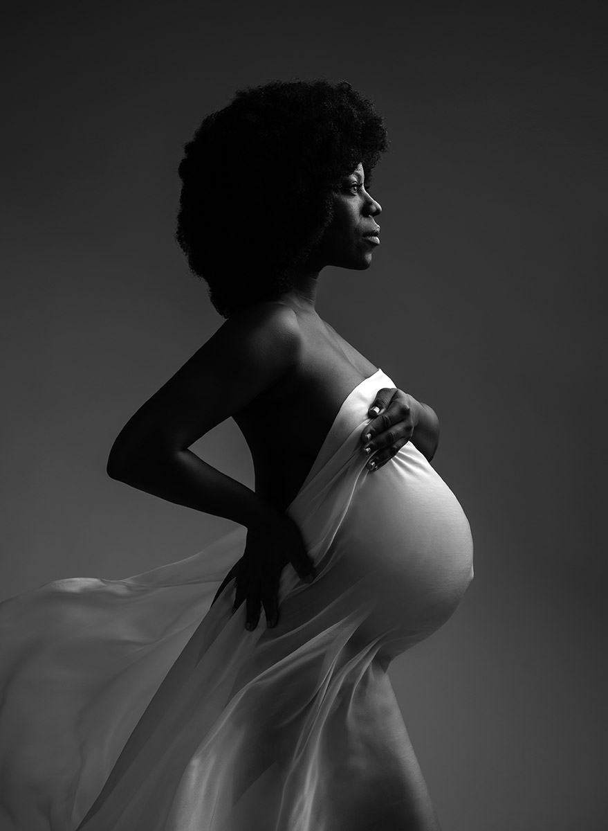 Ethnic woman with afro hair holding a flowing fabric over her pregnant belly