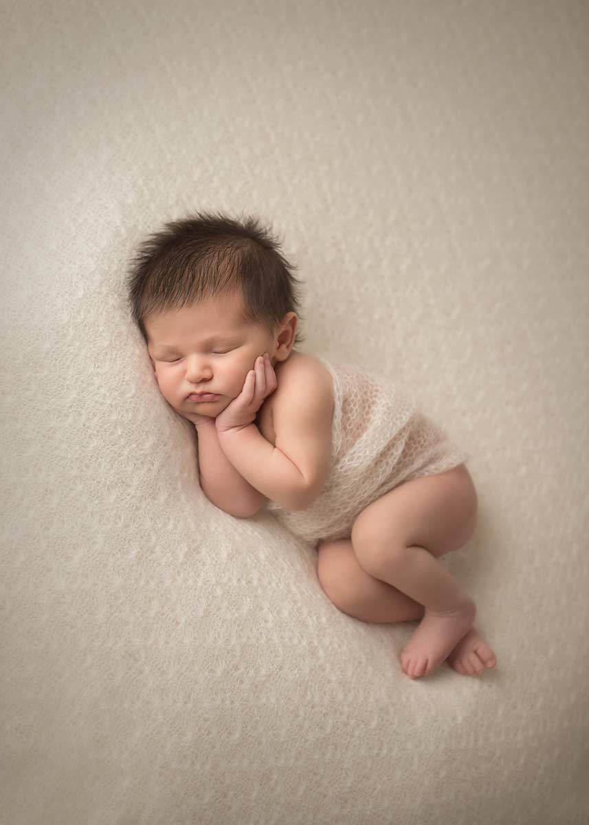NYC Newborn Photographer image of a sleeping infant on a beautiful blanket in a studio