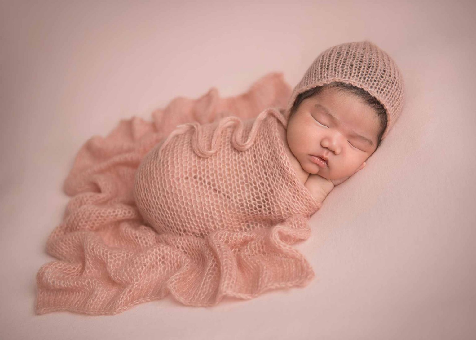 Infant girl sleeping on a pink knit blanket