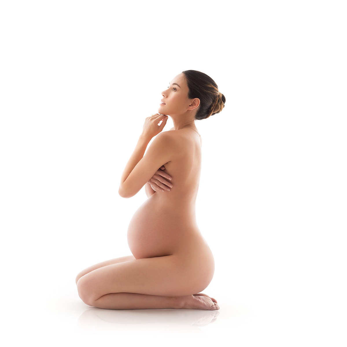Nude woman sitting on the floor and showing off her pregnant belly
