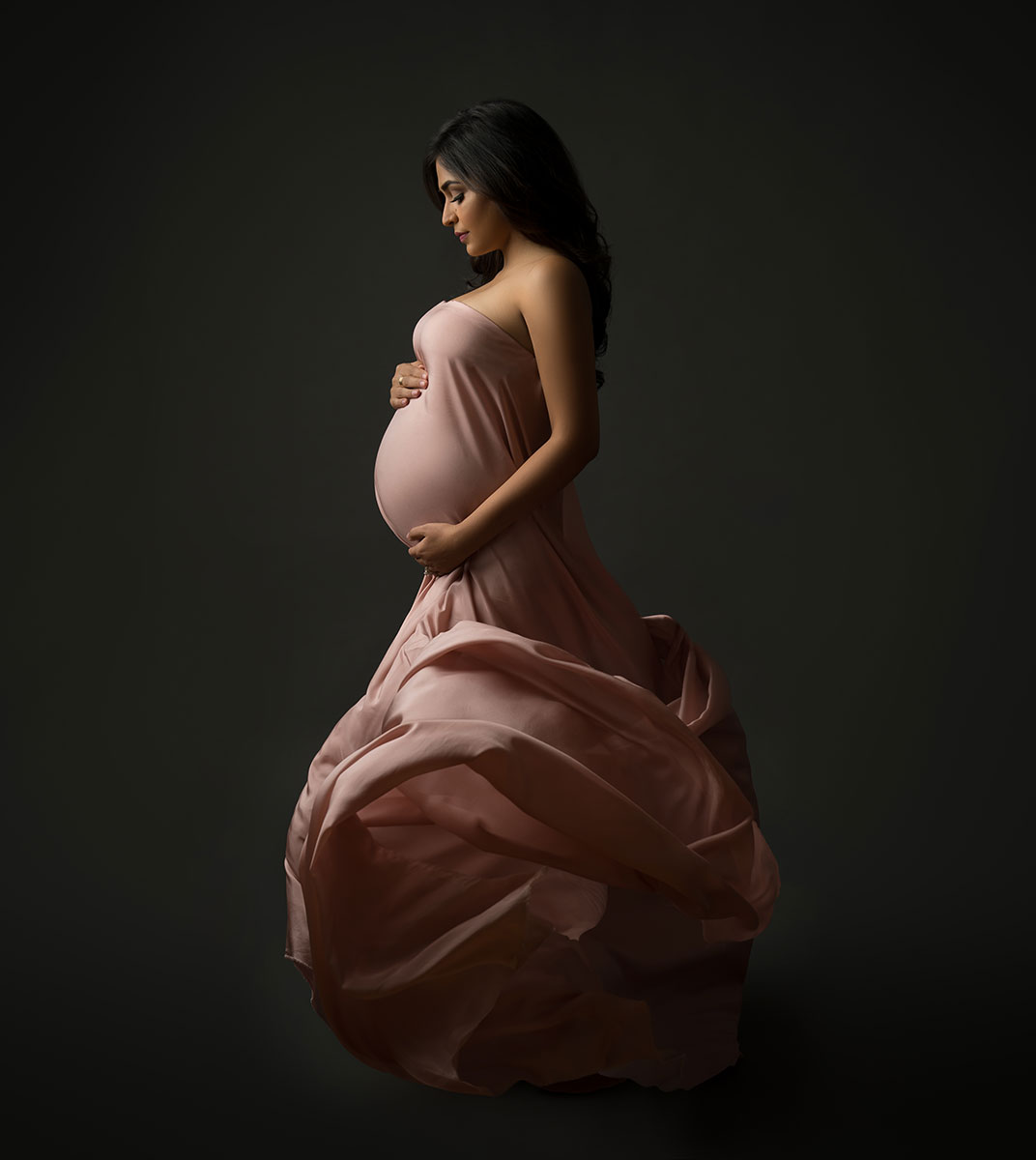 Pregnant woman wearing a flowing pink dress and posing for a portrait