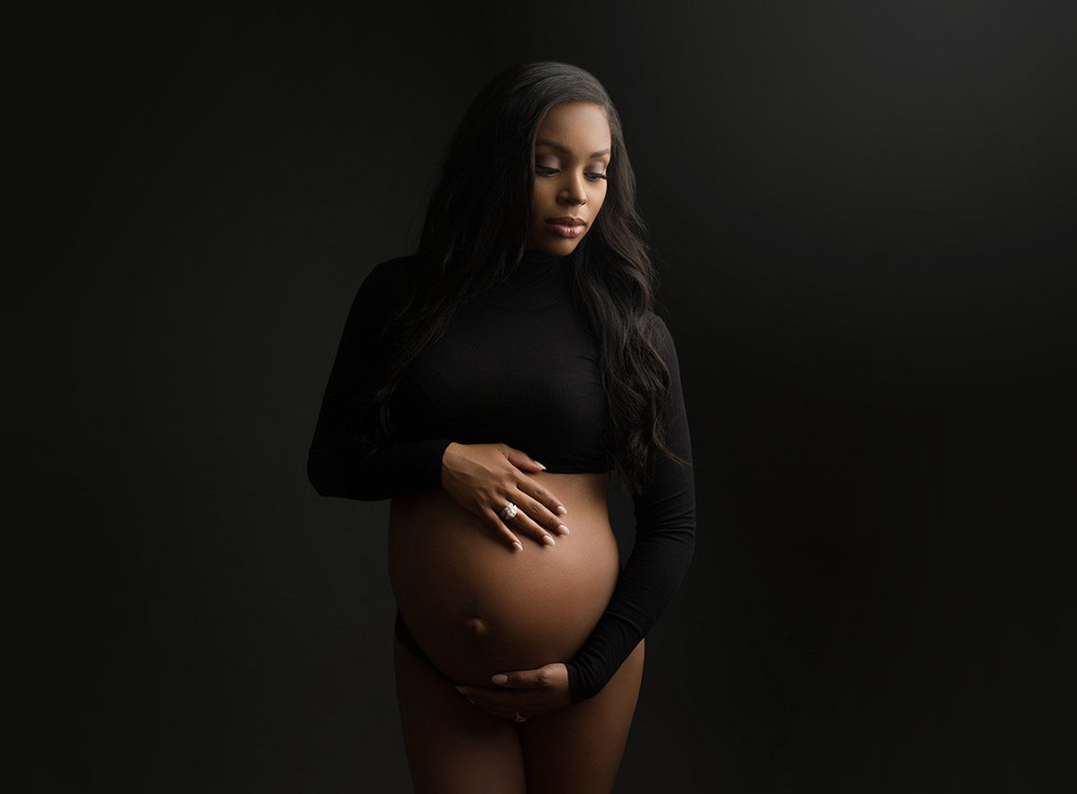 Woman with black hair wearing a crop top and holding her pregnant belly