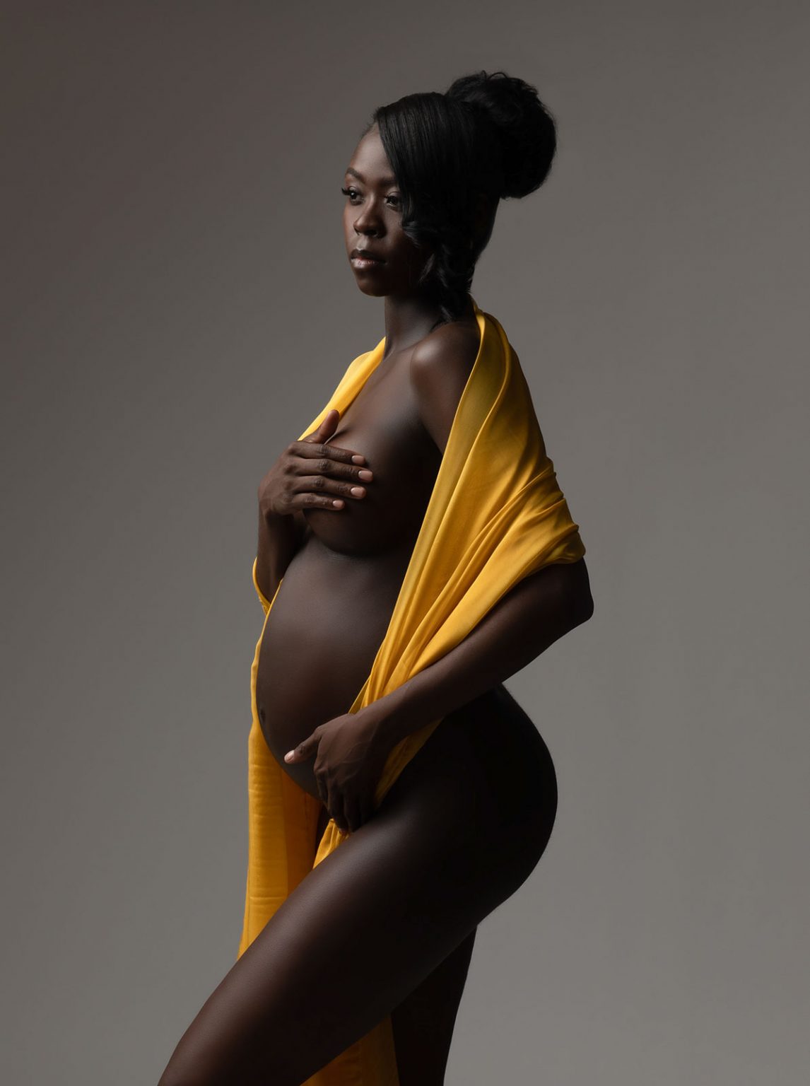 Fine art pregnancy portrait with e;egant hair bun and draped yellow silk