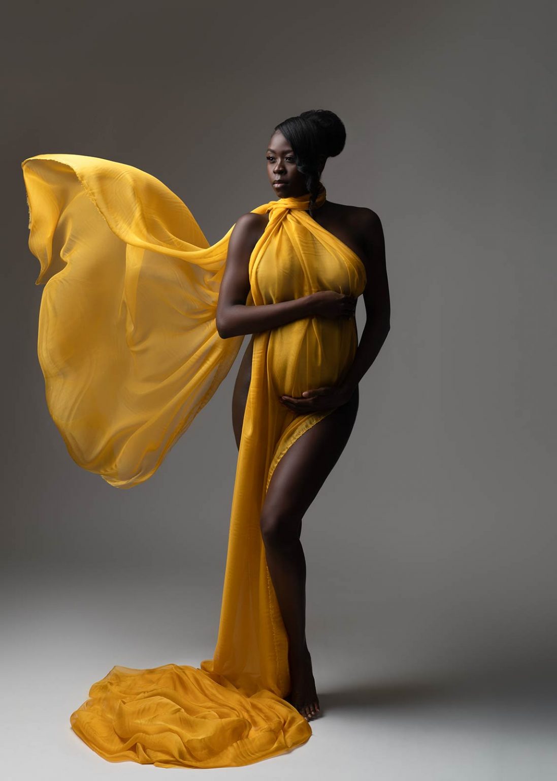 Pregnant woman with elegant hair bun and flying yellow silk