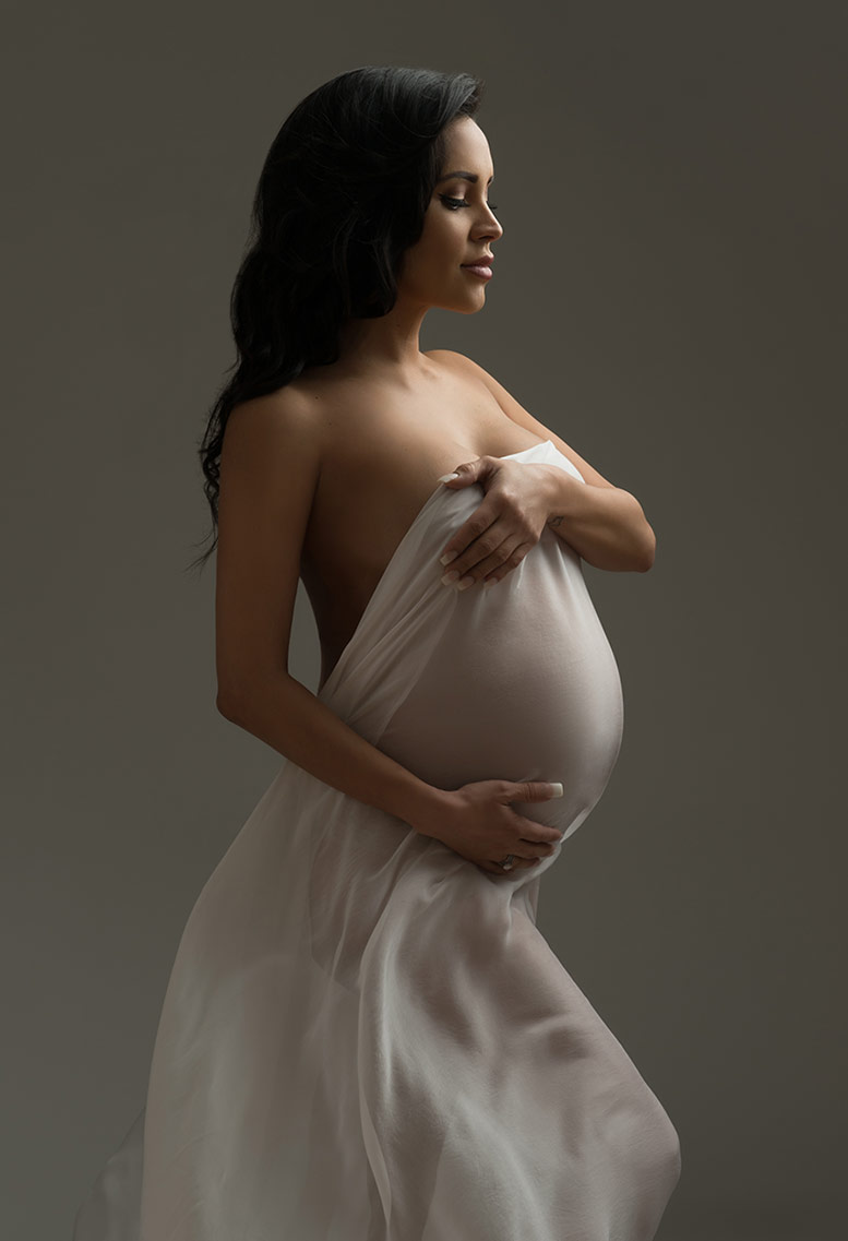 Young pregnant woman holding a fabric over her maternity belly.
