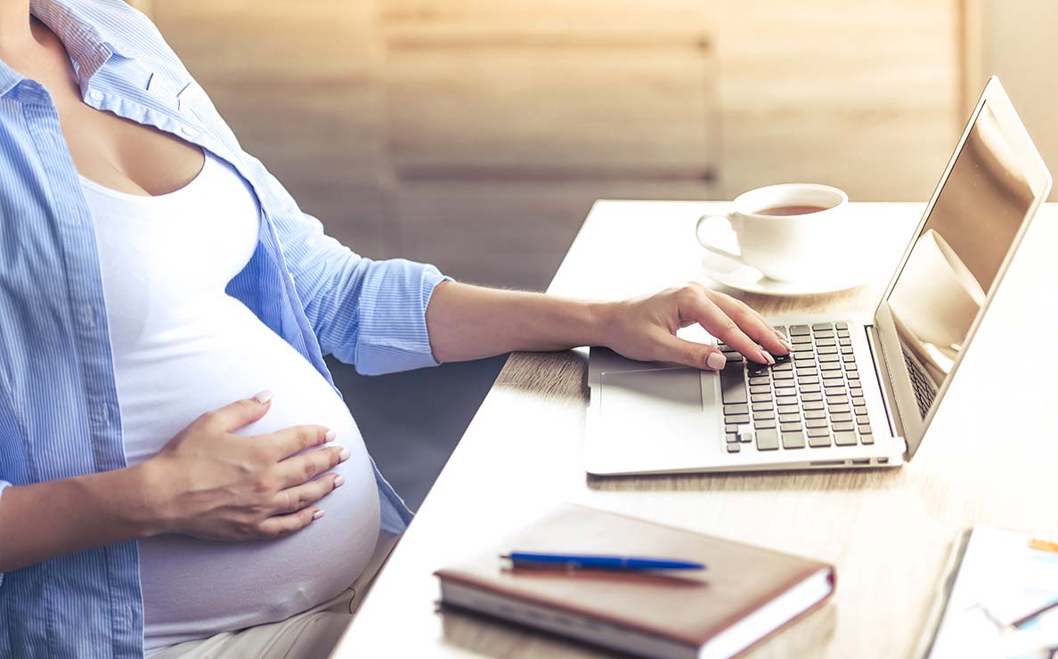Woman holding her pregnant belly while searching on a laptop