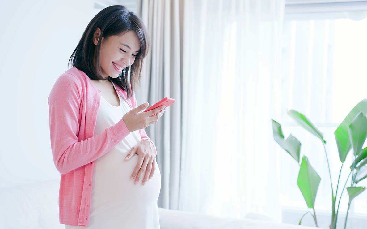 Pregnant woman smiling while holding her phone