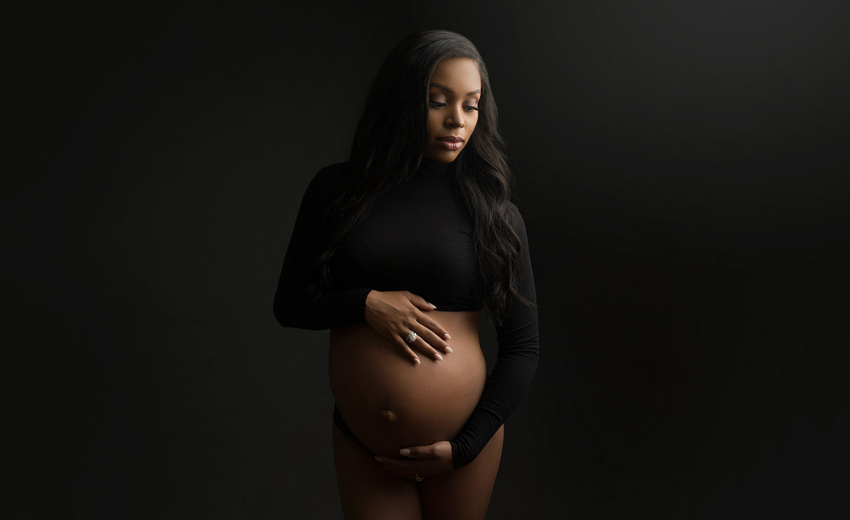 woman with black hair and crop top cradling her pregnant belly