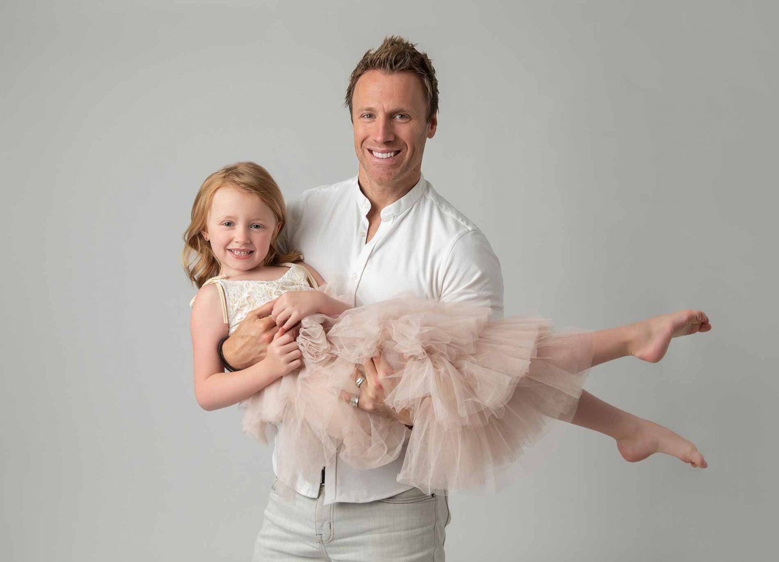Father playfully carrying his daughter in a tutu at a NYC baby photo studio