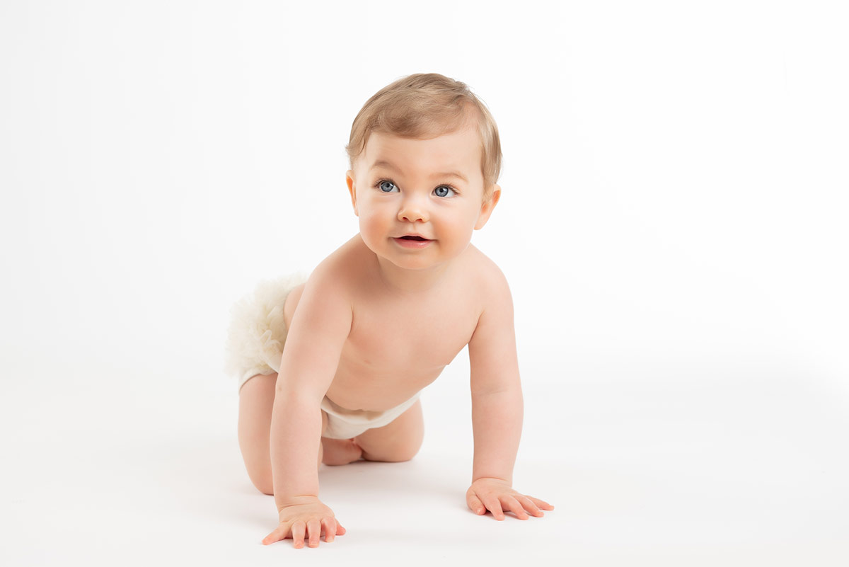 Cute baby in a diaper cover crawling on the floor of a photography studio