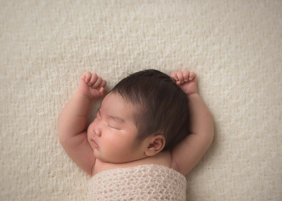 Infant sleeping peacefully with hands up