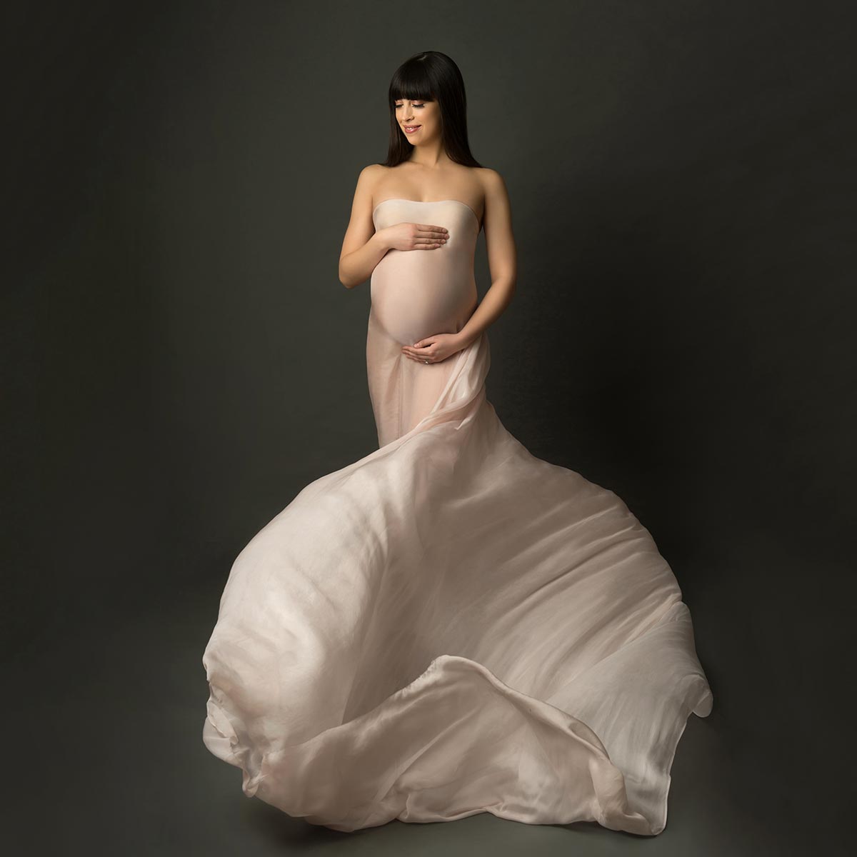 Flying silks surround this pregnant woman posing for a maternity photo