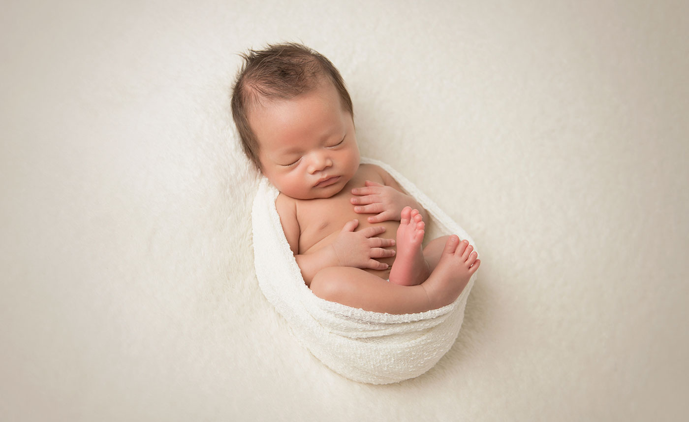 Newborn baby wrapped in a blanket posing for a NYC newborn photographer