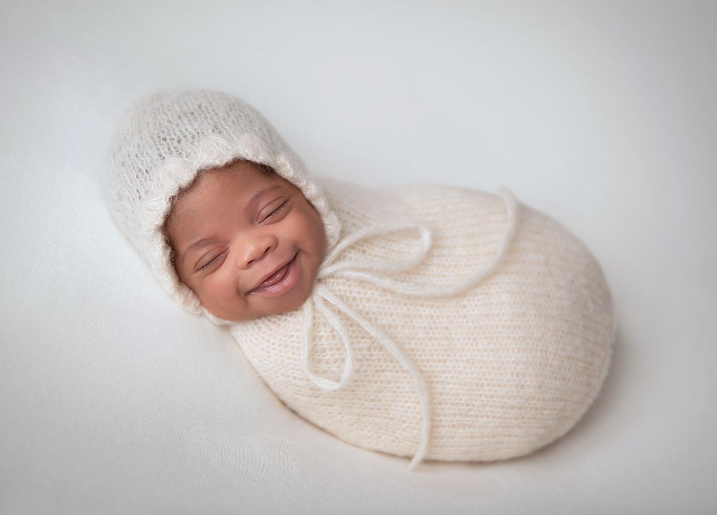 adorable newborn baby with huge smile and cream ruffle bonnet wrap