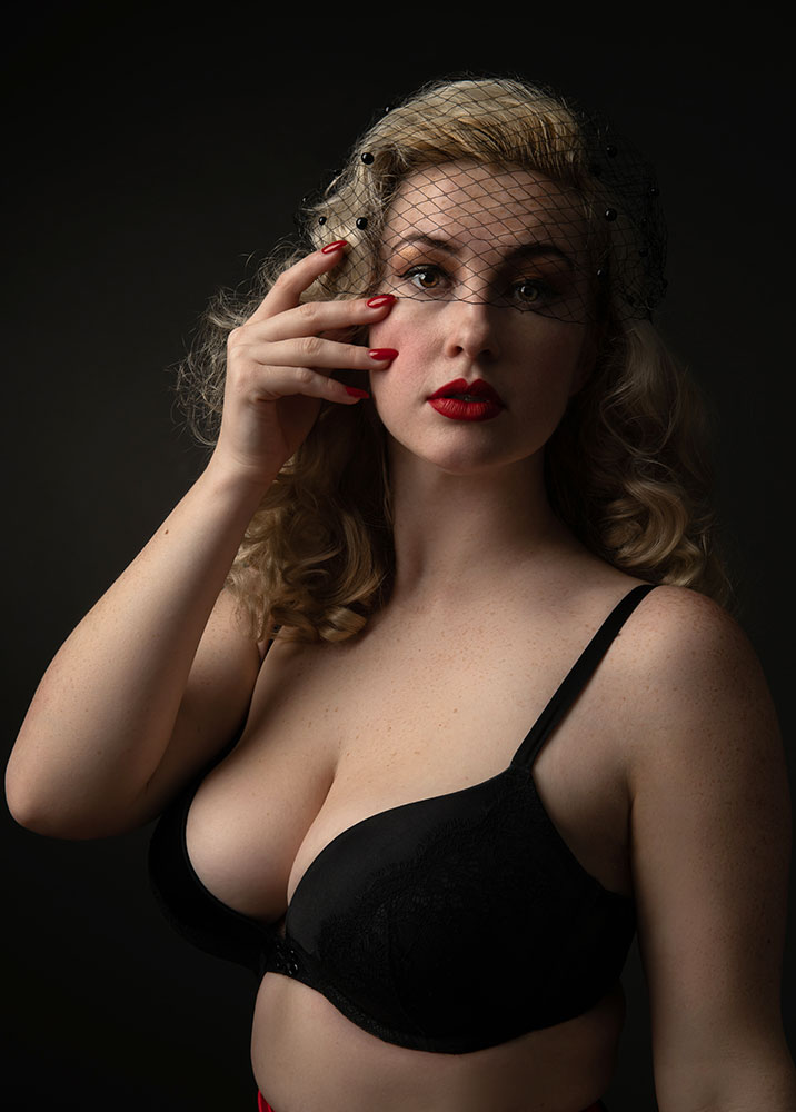 voluptuous blonde bombshell wearing black lingerie and fishnet hair accessory for boudoir photoshoot