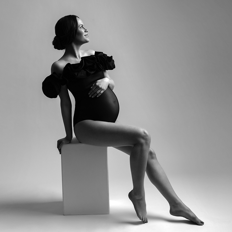 black and white image of pregnant woman on studio posing stool