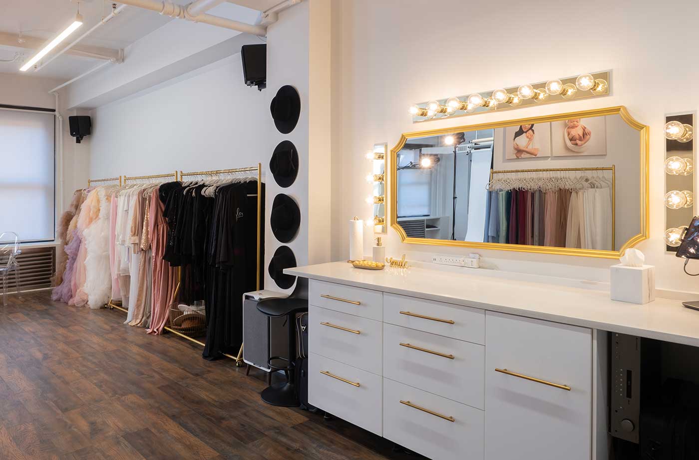 Make-up and hair styling table at a photography studio. Adjacent stands a wardrobe rack with an assortment of maternity dresses.